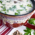 Wild rice soup in a red bowl with wild rice on the table next to it.