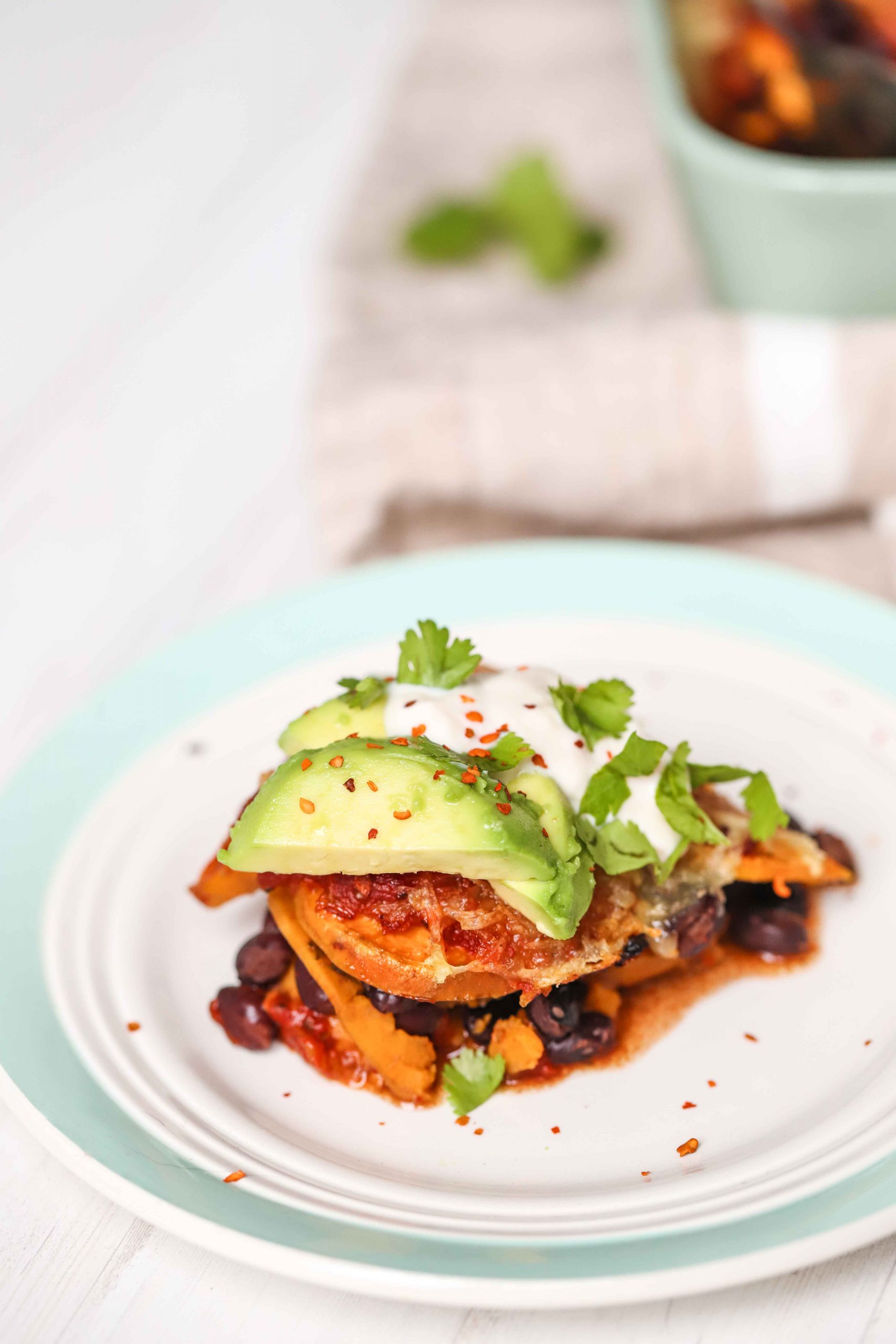 a piece of sweet potato and black bean casserole on a green and white plate garnished with avocado and red pepper flakes