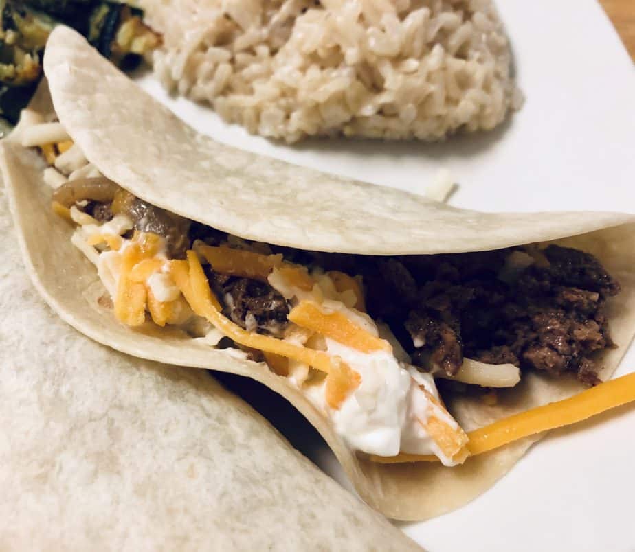 flour tortilla shell with steak, sour cream and cheddar cheese on a white plate 