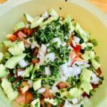 chopped up tomatoes, avocado, onions, peppers and chickpeas in a green bowl with cilantro on top