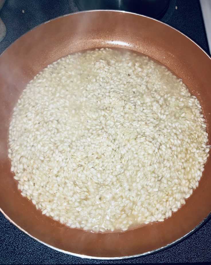 risotto that is just starting to cook, in a copper pan, with some steam rising up