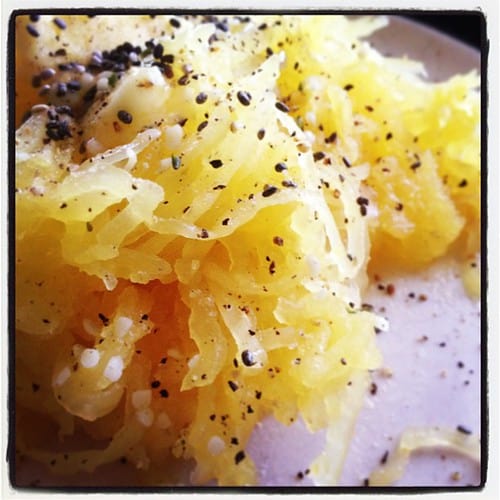 A super close-up pile of spaghetti squash on a pink plate, with salt and pepper on it. 