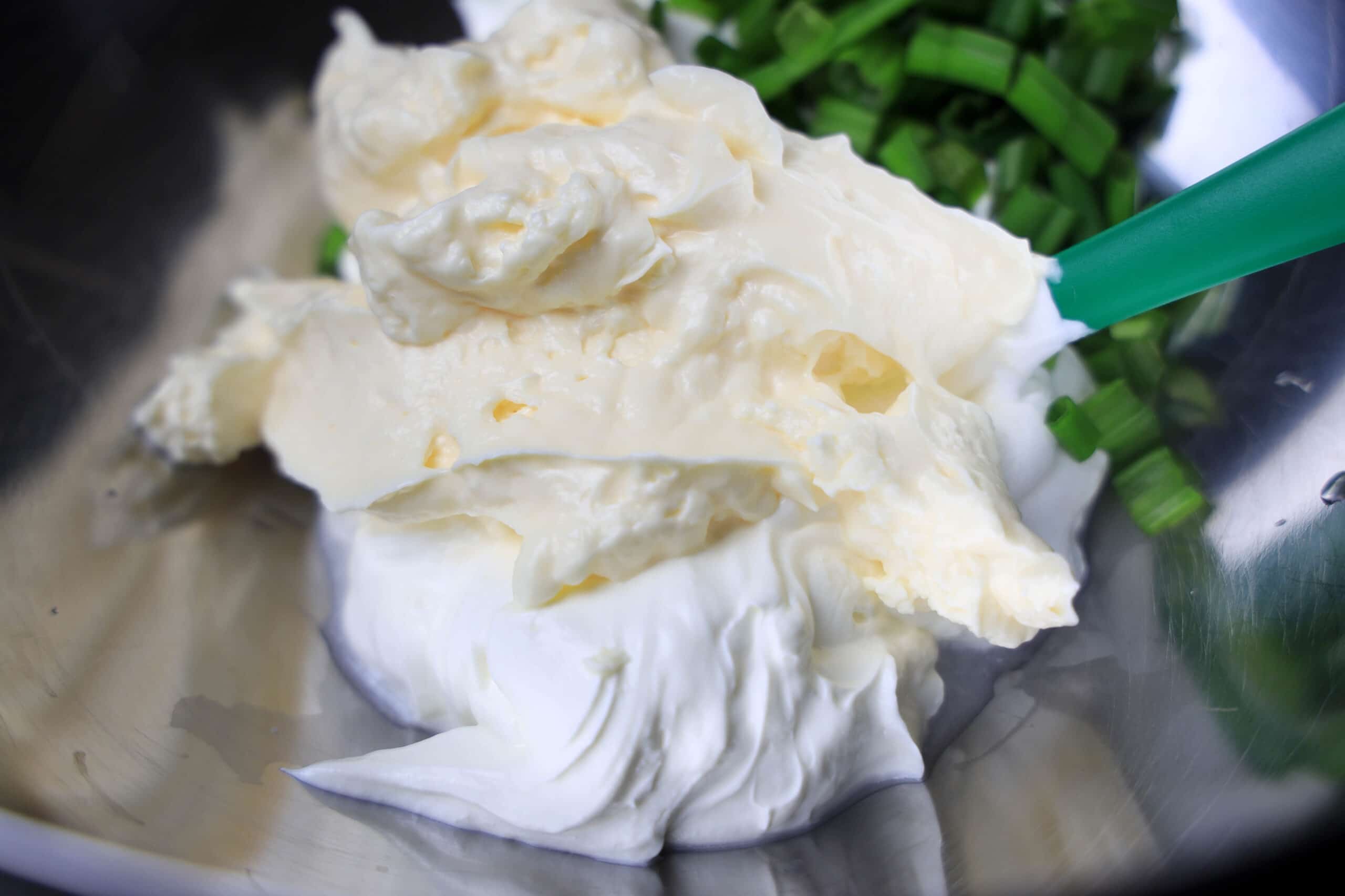 Mayo on a spoon with green onions in the background