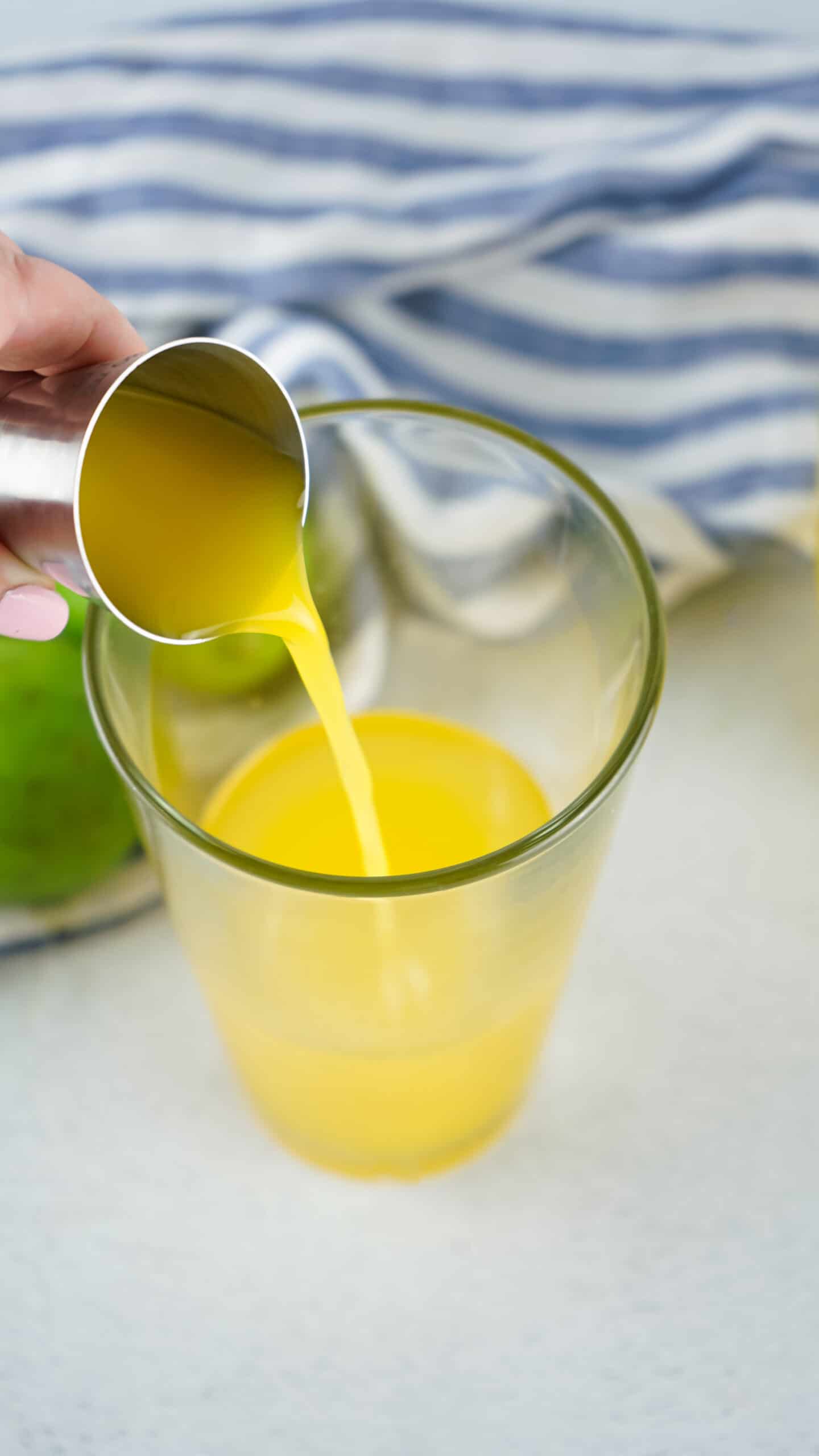 Pineapple juice being poured from a measuring cup into a glass