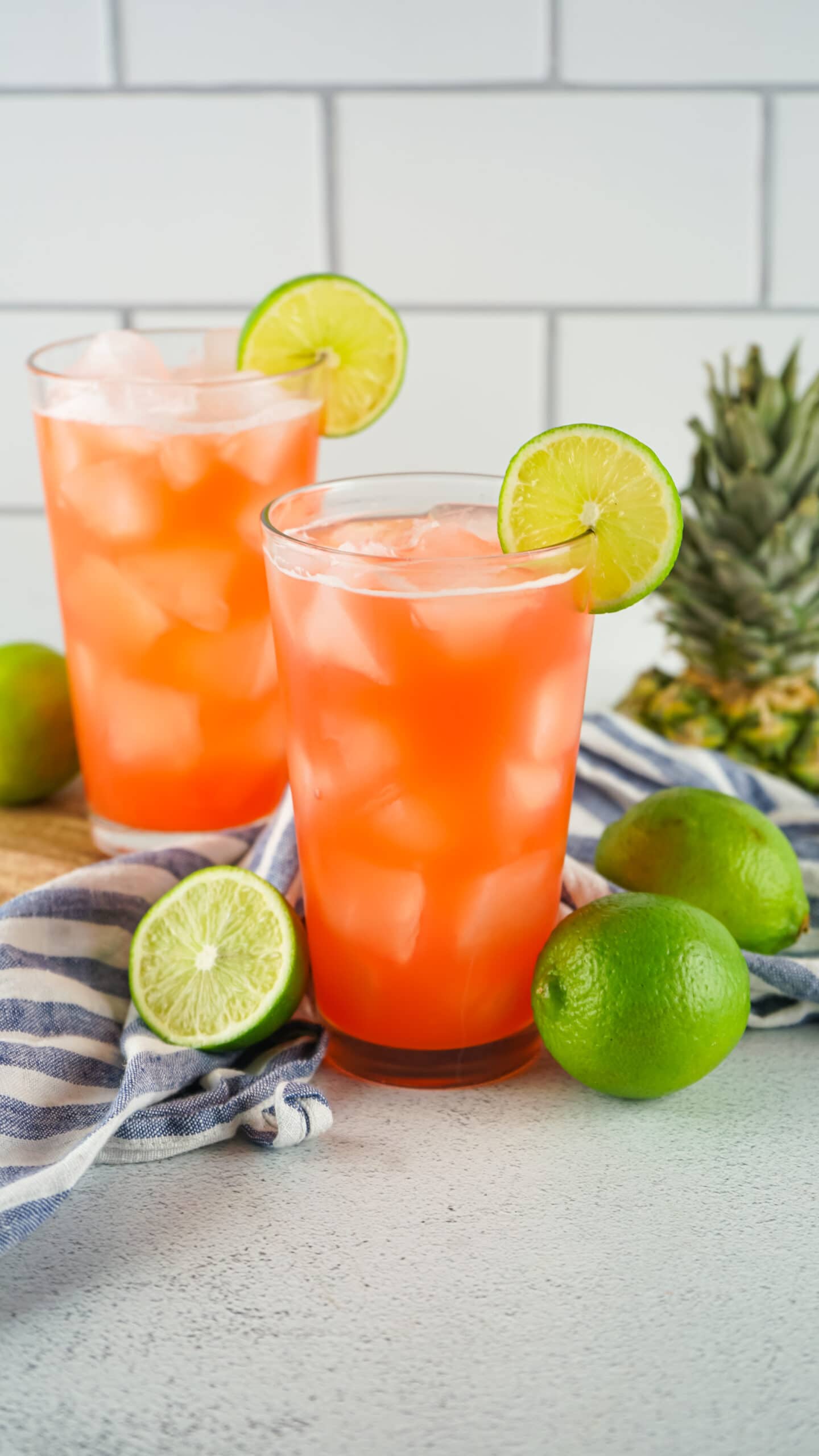 2 drinks glasses with lime slices and limes on a table.